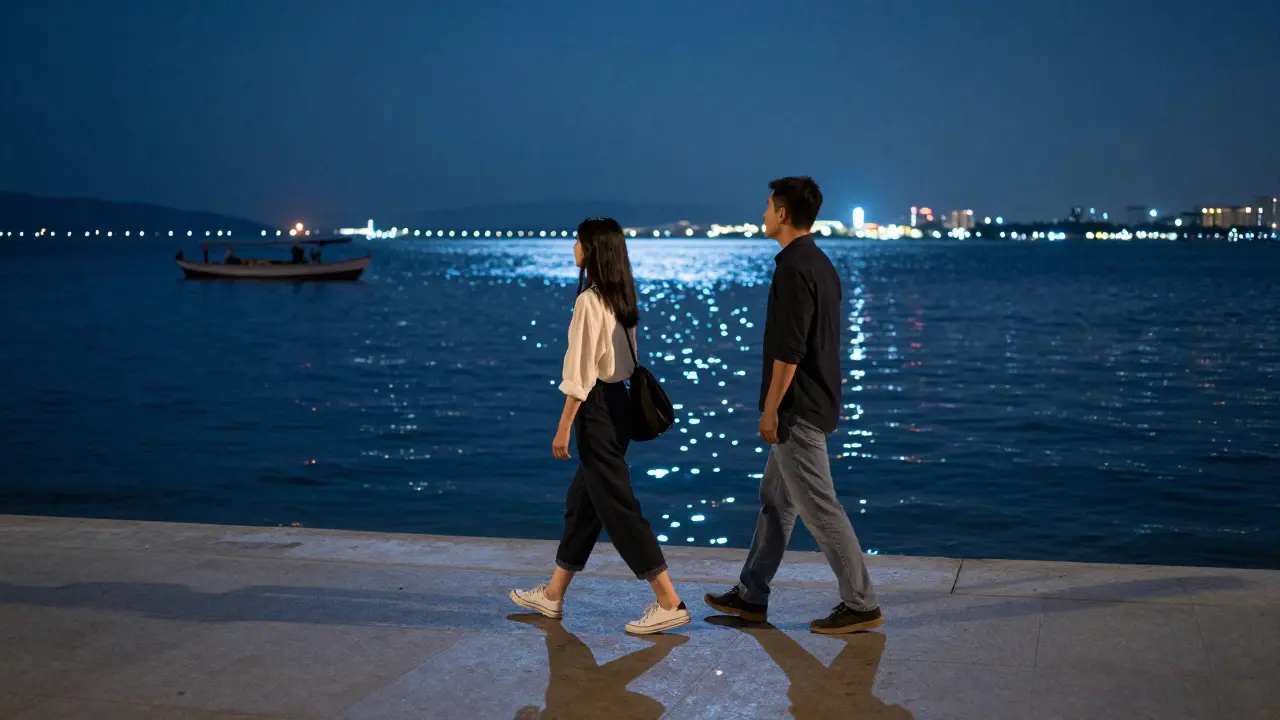 Two people walking silently along the Corniche at midnight, city lights reflecting on water.